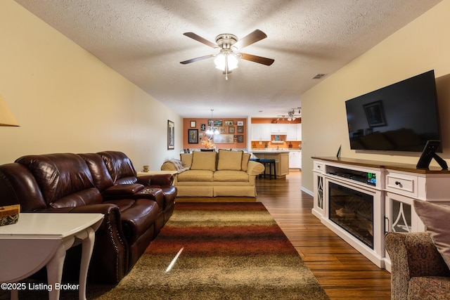 living area featuring ceiling fan, visible vents, dark wood finished floors, and a textured ceiling