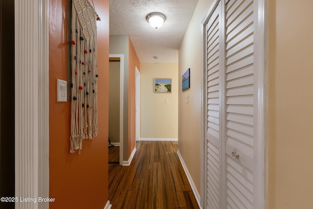 hallway featuring dark wood-style flooring, a textured ceiling, and baseboards