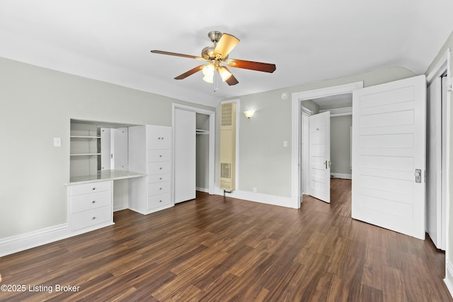 unfurnished bedroom featuring a ceiling fan, built in study area, dark wood finished floors, and baseboards