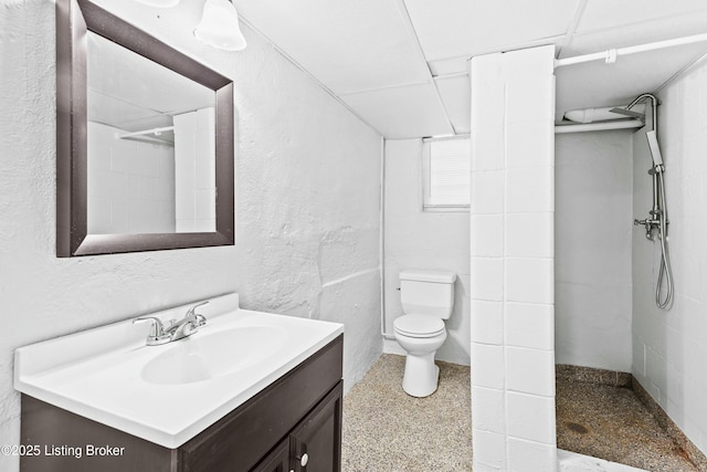 bathroom with toilet, a textured wall, a tile shower, and vanity