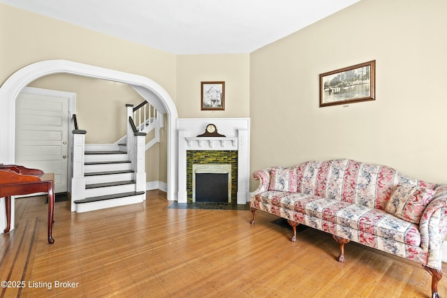 living room with stairs, a tile fireplace, arched walkways, and wood finished floors