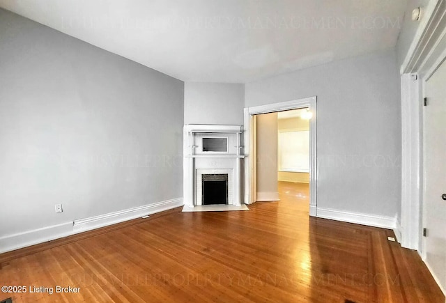 unfurnished living room featuring a fireplace with flush hearth, baseboards, and wood finished floors