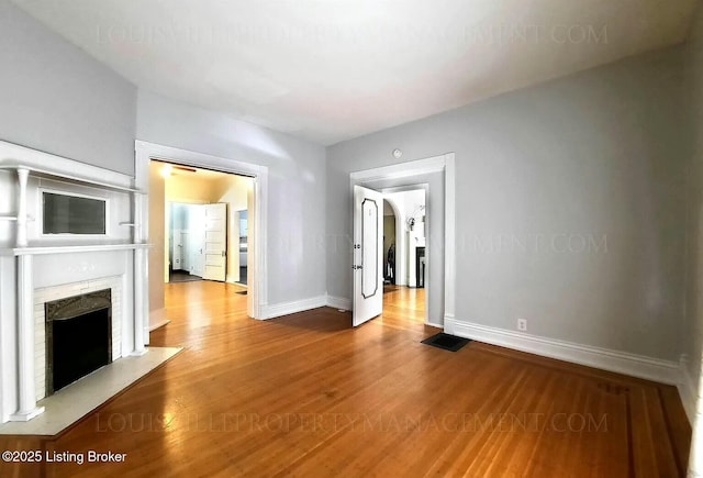 unfurnished living room featuring a fireplace with flush hearth, baseboards, and wood finished floors