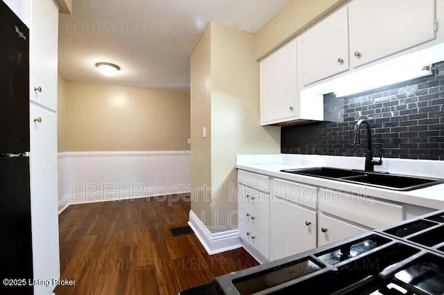 kitchen featuring a sink, white cabinets, light countertops, backsplash, and dark wood finished floors