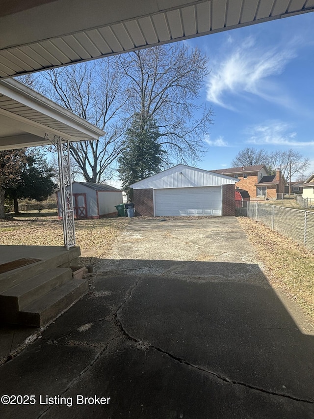 exterior space featuring a garage, driveway, fence, and an outdoor structure