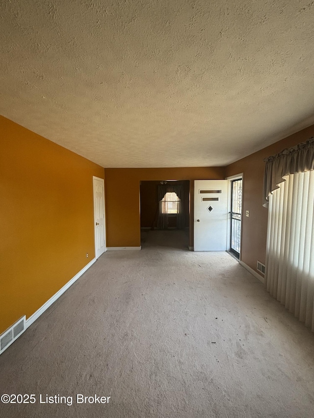 unfurnished living room featuring light carpet, a textured ceiling, visible vents, and baseboards