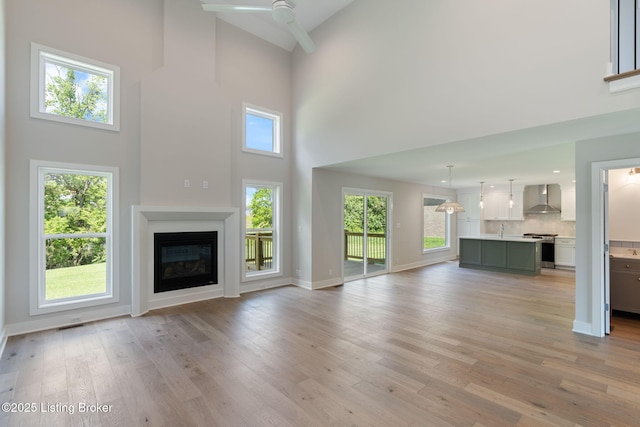 3314 Catalpa Farms Dr, Fisherville, KY 40023 - unfurnished living room featuring a towering ceiling, ceiling fan, light wood-style floors, a glass covered fireplace, and a sink