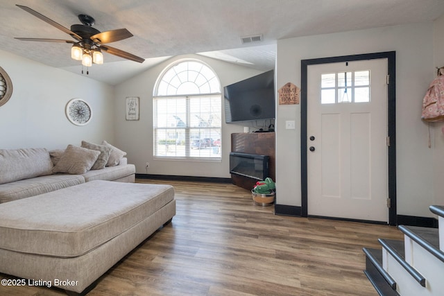 living area with lofted ceiling, wood finished floors, visible vents, baseboards, and a glass covered fireplace