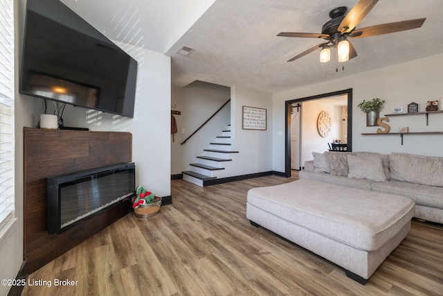 living room featuring a glass covered fireplace, a textured ceiling, wood finished floors, baseboards, and stairs