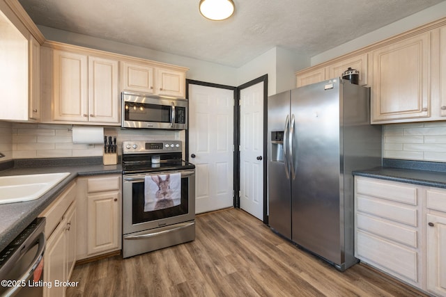 kitchen featuring dark countertops, wood finished floors, a sink, stainless steel appliances, and backsplash