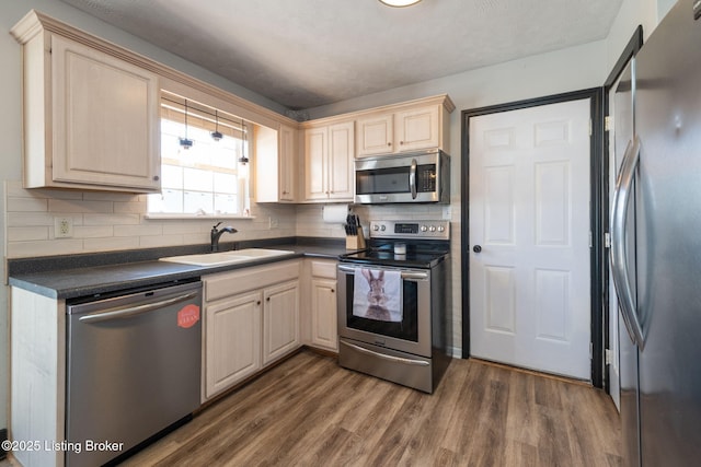 kitchen with dark countertops, appliances with stainless steel finishes, dark wood finished floors, and a sink