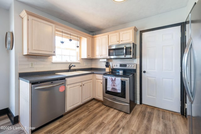 kitchen featuring stainless steel appliances, wood finished floors, dark countertops, and a sink