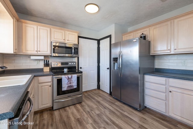 kitchen with dark countertops, backsplash, appliances with stainless steel finishes, a sink, and wood finished floors