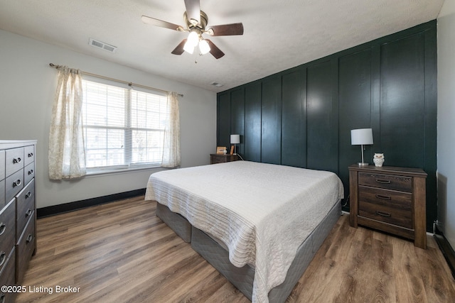 bedroom featuring a ceiling fan, wood finished floors, visible vents, and baseboards