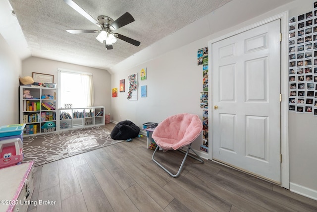 playroom featuring lofted ceiling, a textured ceiling, baseboards, and wood finished floors