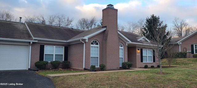 view of front of property featuring brick siding, aphalt driveway, a front yard, a chimney, and a garage