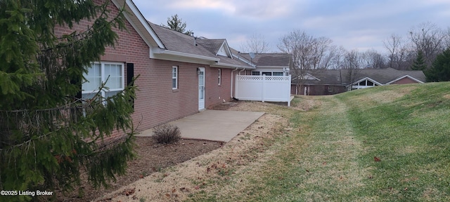 view of side of home featuring brick siding, a lawn, a patio, and fence