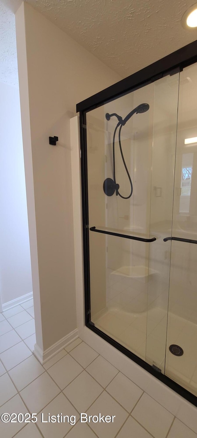 bathroom with a textured ceiling, a stall shower, tile patterned flooring, and baseboards