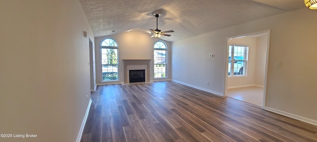 unfurnished living room with dark wood-style flooring, a glass covered fireplace, vaulted ceiling, a textured ceiling, and baseboards