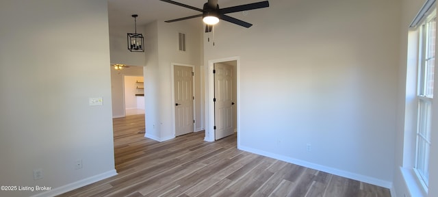 unfurnished room featuring visible vents, baseboards, a ceiling fan, wood finished floors, and a high ceiling