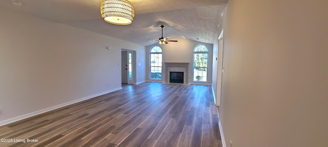 unfurnished living room with a tile fireplace, a ceiling fan, baseboards, vaulted ceiling, and dark wood finished floors