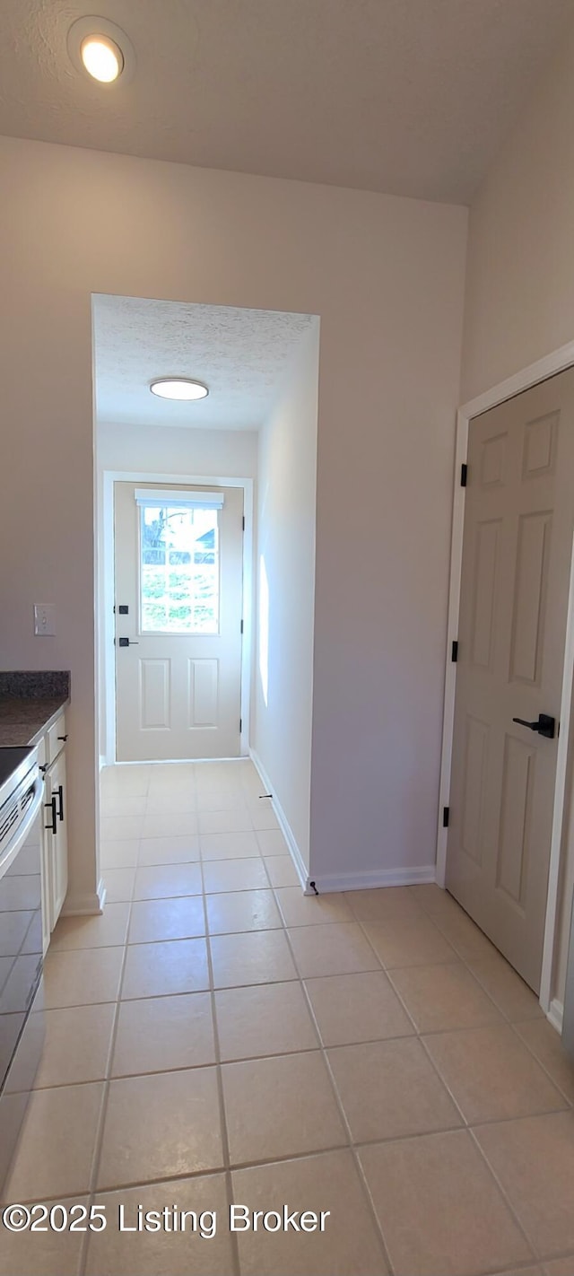 corridor featuring light tile patterned flooring, a textured ceiling, and baseboards