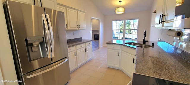 kitchen with a sink, stainless steel fridge, white cabinetry, and lofted ceiling