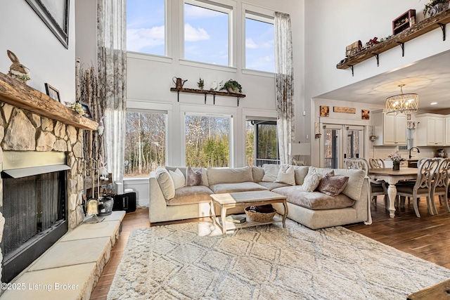 living room featuring a notable chandelier, a high ceiling, wood finished floors, and a stone fireplace