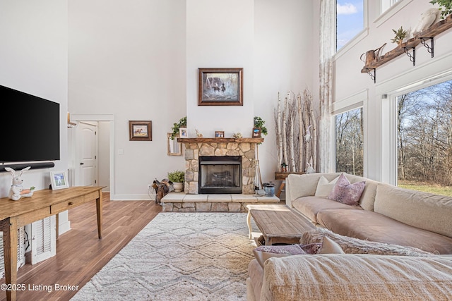 living area with a fireplace, a towering ceiling, baseboards, and wood finished floors