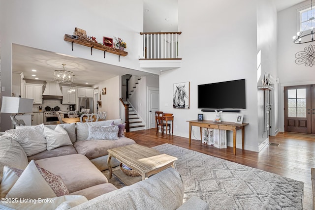 living room featuring a notable chandelier, wood finished floors, a towering ceiling, baseboards, and stairs