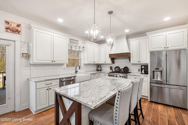 kitchen featuring appliances with stainless steel finishes, a sink, wood finished floors, premium range hood, and a kitchen breakfast bar