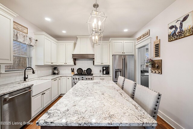 kitchen featuring decorative backsplash, custom range hood, high quality appliances, a center island, and a sink