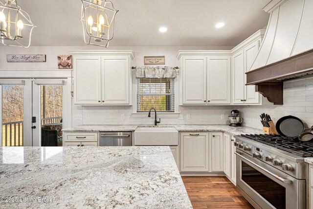 kitchen with stainless steel appliances, wood finished floors, a sink, backsplash, and custom range hood