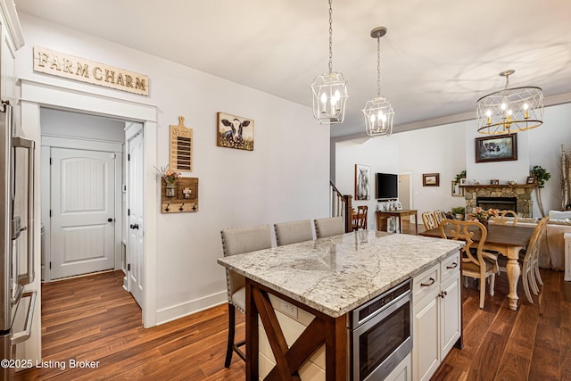 kitchen with pendant lighting, dark wood finished floors, stainless steel microwave, white cabinets, and light stone countertops