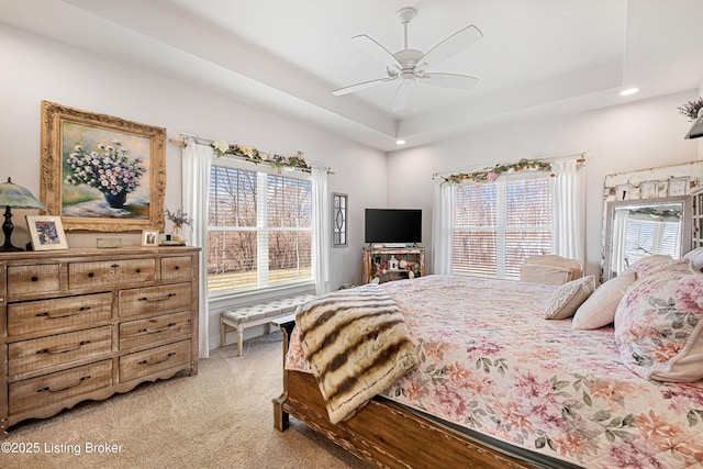 bedroom with ceiling fan, a tray ceiling, and light colored carpet