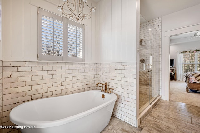 bathroom with a chandelier, a stall shower, a freestanding tub, and tile walls