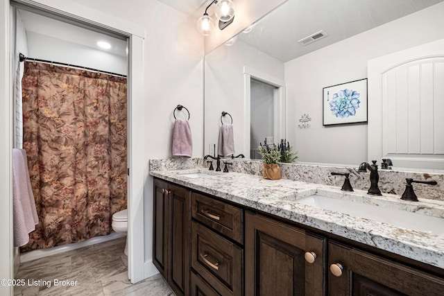 bathroom featuring toilet, double vanity, a sink, and visible vents