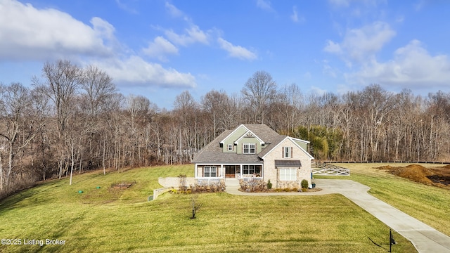 view of front of house with covered porch, driveway, stone siding, a forest view, and a front lawn