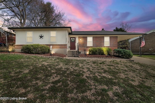 view of front facade with a carport, concrete driveway, a yard, and brick siding