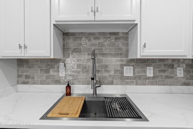 kitchen featuring tasteful backsplash, white cabinetry, light stone counters, and a sink