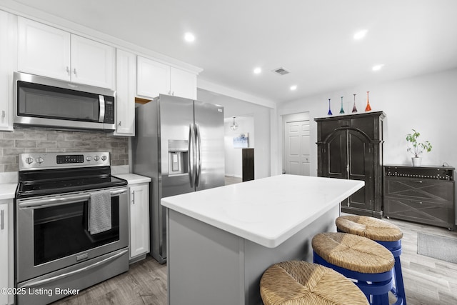 kitchen featuring visible vents, a kitchen island, stainless steel appliances, light countertops, and decorative backsplash