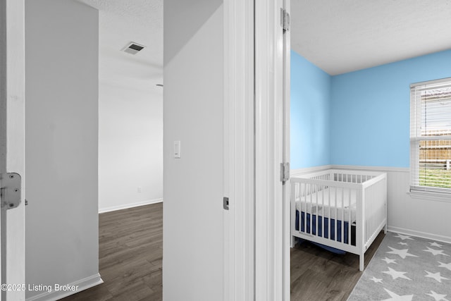 bedroom featuring visible vents, a crib, a wainscoted wall, wood finished floors, and a textured ceiling