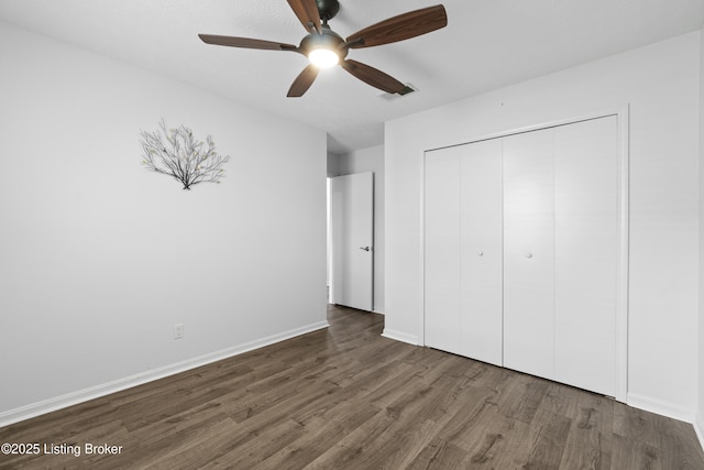 unfurnished bedroom featuring dark wood-style floors, visible vents, baseboards, ceiling fan, and a closet