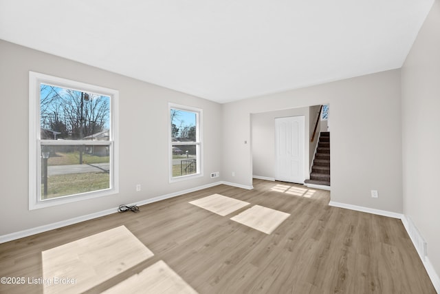 unfurnished room featuring stairway, wood finished floors, visible vents, and baseboards