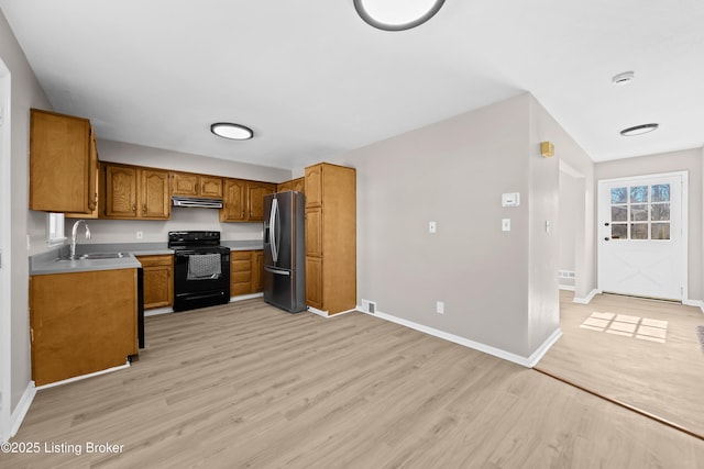 kitchen featuring black / electric stove, under cabinet range hood, a sink, brown cabinetry, and stainless steel fridge