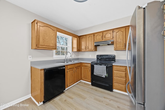 kitchen with light wood-style flooring, under cabinet range hood, a sink, light countertops, and black appliances