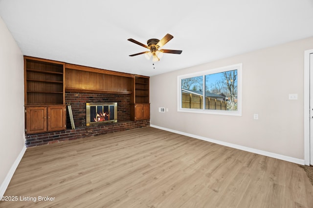 unfurnished living room with built in shelves, a fireplace, light wood-style flooring, and baseboards