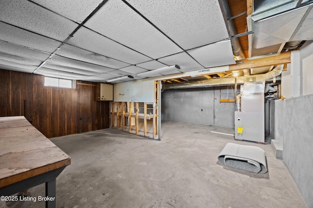 below grade area with heating unit, wood walls, and a drop ceiling