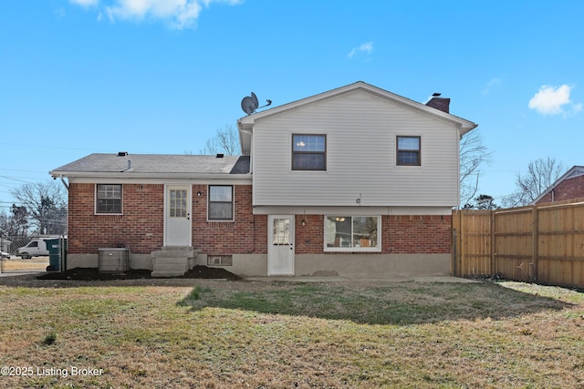 rear view of property featuring entry steps, fence, a lawn, and brick siding