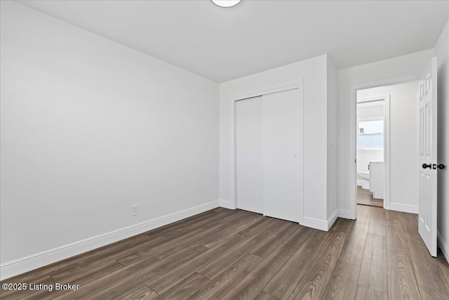 unfurnished bedroom featuring baseboards, dark wood-style flooring, and a closet